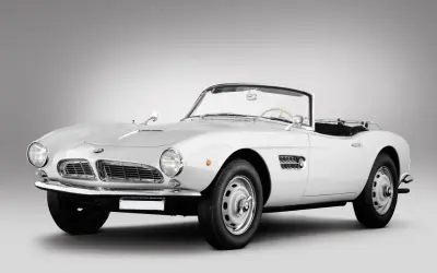 Biały kabriolet BMW 507 z lat 50. prezentuje się elegancko na szarym tle.