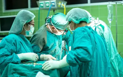 Zespół chirurgów w sterylnych strojach pracuje przy stole operacyjnym. W tle widać aparaturę medyczną. Sytuacja budzi niepokój, czy nieumyślne spowodowanie śmierci nie jest tu możliwe.