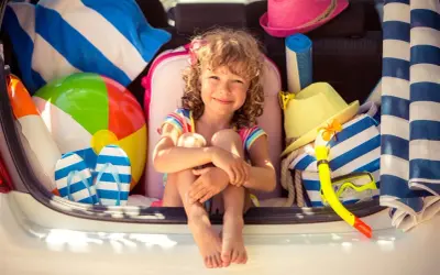 Niña sonriente rodeada de artículos de playa, lista para explorar nuevos sitios para ir con niños.
