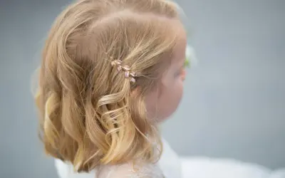 Urocze fryzury ze spinką z boku, ozdobioną listkami, dodają blasku blond włosom dziewczynki.