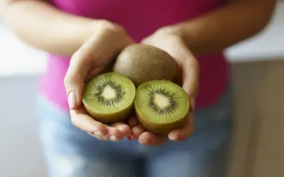 Dłonie trzymają całe i przekrojone kiwi. Ten owoc to naturalny sposób na zaparcia.