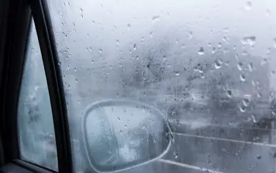 Gotas de lluvia en el cristal del coche, reflejando el exterior y el espejo retrovisor. Una escena que explica porque se empañan los cristales en días húmedos.