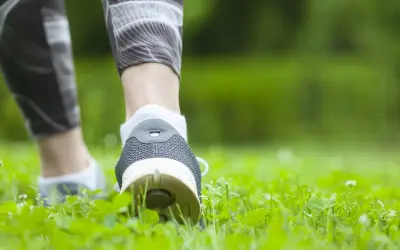 Füße in Sportschuhen und Laufhose bewegen sich durch grünes Gras. Spazieren gehen ist Sport und gut für die Gesundheit.