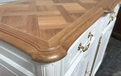 Un meuble ancien relooké en moderne, avec un plateau en bois clair à motif géométrique et des poignées dorées sur un corps blanc.