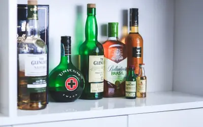 Rząd butelek z alkoholami, w tym Unicum i różne whisky, jakby zapomniane nalewki czekające na degustację.