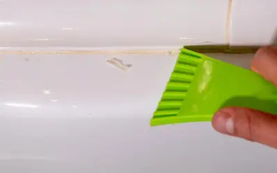 Outil vert raclant du mastic durci sur une surface blanche.