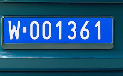 Niebieskie tablice rejestracyjne z numerem W-001361 na ciemnozielonym samochodzie.