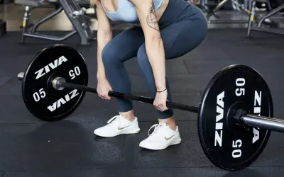 Donna in palestra si prepara per gli stacchi da terra con un bilanciere.