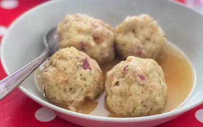Canederli in brodo, uno dei piatti tipici del Trentino Alto Adige, serviti in una ciotola bianca su un tovagliolo rosso a pois bianchi.