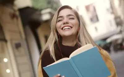 Uśmiechnięta dziewczyna z książką i słuchawkami na ulicy. Może to być studentka, która właśnie skończyła lekcje w szkole w Danii.