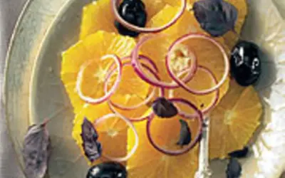 Erfrischender Salat mit Orangen, roten Zwiebelringen, schwarzen Oliven und dunklen Kräutern auf einem Teller.