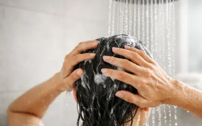 Mani che massaggiano shampoo sui capelli scuri sotto la doccia. Lavare i capelli tutti i giorni fa male, meglio farlo meno spesso.