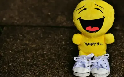 Żółta maskotka z napisem "Happy..." i śmiesznymi cytatami na twarzy, w białych trampkach.