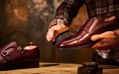 Un uomo lucida scarpe in pelle bordeaux con una spazzola, un rituale per mantenerle splendenti.