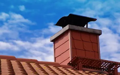 Ein roter Ziegelschornstein mit schwarzer Haube unter blauem Himmel. Die Vorbereitung, einen alten Schornstein wieder in Betrieb zu nehmen, ist sichtbar.