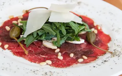 Delicato carpaccio di manzo con rucola, scaglie di parmigiano, pinoli, capperi e funghi champignon.
