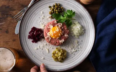 En tallrik med råbiff, äggula, kapris, hackad lök, rödbetor och gurka. Perfekt för ett klassiskt råbiff recept.