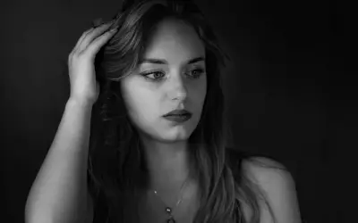 Portret młodej kobiety w odcieniach **black color**. Jej dłoń spoczywa na włosach, a wzrok skierowany jest w bok, w głąb mroku.