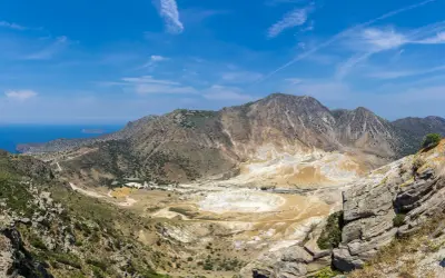 Krajobraz wulkaniczny Nisyros z kraterem pokrytym osadami i górami w tle.
