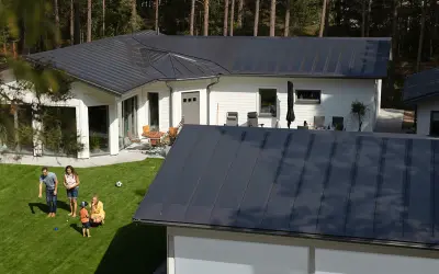 Familj njuter av solen på gräsmattan framför ett modernt hus med ett stilrent lindab solar roof.