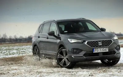 Szary Seat Tarraco SUV przemierza błotniste, zaśnieżone pole, wzbijając chmury brudu.