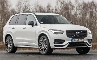 Białe Volvo XC90 T6 z czarnymi felgami stoi na drodze, za nim las.