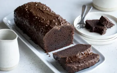 Un généreux gâteau au chocolat haut, nappé d'un glaçage croquant et parsemé de noisettes. Deux tranches sont déjà coupées, prêtes à être dégustées.