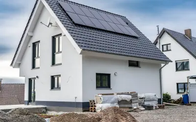 Nowy dom z panelami słonecznymi na dachu, w trakcie rozbudowy. Wokół materiały budowlane.