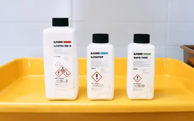 Three Ilford bottles for developing, stopping, and fixing film sit in a yellow tray, ready for creating the best black and white film.