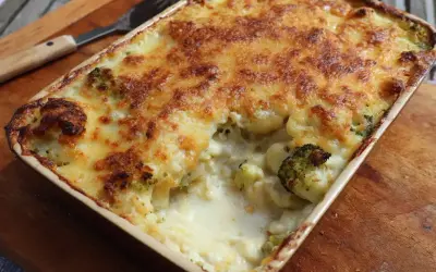 En ugnsform med ostgratinerad blomkål och broccoli, gyllene och bubblande. En sked ligger bredvid.