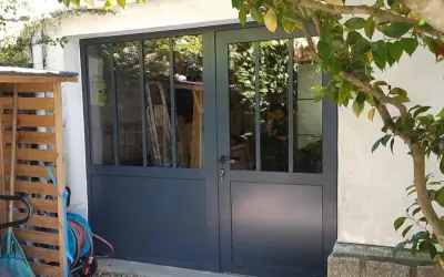 Remplacer porte de garage par fenêtre : une nouvelle entrée lumineuse avec des portes vitrées grises. Des outils de jardin sont rangés à gauche.