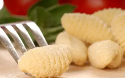 Une fourchette pique un gnocchi fait maison, prêt pour une délicieuse recette gnocchi. Des gnocchis frais et des ingrédients italiens en arrière-plan.