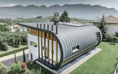 Nowoczesny dom z zaokrąglonym dachem z aluminium, które nie koroduje, otoczony zielenią i górami.