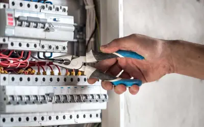 Elektryk z kombinerkami przy skrzynce z bezpiecznikami, przygotowuje się, jak włączyć prąd.