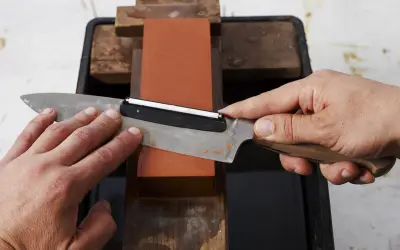 Händer slipar en kniv mot en orange sten. En vass kniv är viktig för matlagning.