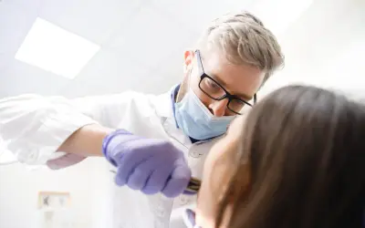 Dentysta w masce i rękawiczkach wykonuje borowanie zęba pacjentowi.