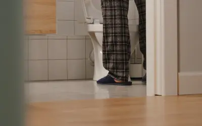 Osoba w piżamie stoi przy toalecie, widać jej nogi i kapcie. Czyżby pojawiły się bąbelki w moczu?