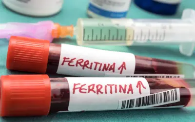 Dwie probówki z krwią oznaczone "Ferritina" i strzałką w górę, sugerujące potrzebę podniesienia ferrytyny. W tle strzykawka i fiolki.