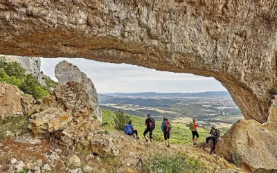 Senderismo Navarra: grupo de excursionistas admira un paisaje montañoso desde debajo de un arco de roca natural.