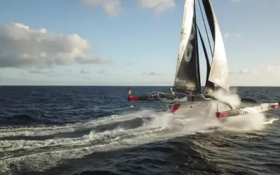 Le trimaran "Actual" d'Yves Le Blevec fend les vagues, propulsé par le vent sous un ciel bleu.
