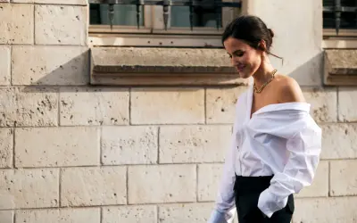 Donna con camicia bianca oversize e pantaloni neri, un look smart casual con una collana dorata.
