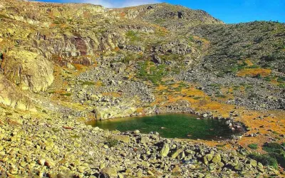Laguna en la ruta de Peñalara, rodeada de rocas y vegetación de montaña bajo un cielo azul.