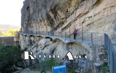 Un pontón de la oliva, parte de la Ruta del Agua, se aferra a un acantilado rocoso. Una mujer camina por el sendero con barandillas.
