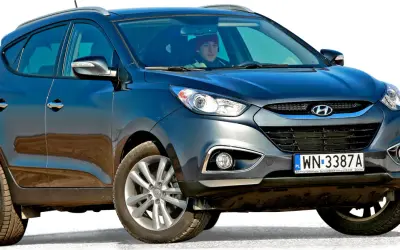 Ciemnoszary Hyundai Tucson, jeden z popularnych koreańskich samochodów, z kierowcą w czerwonej czapce za kierownicą.