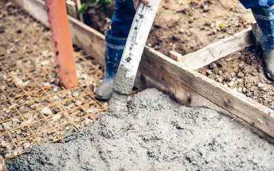 Arbeiter betonieren bei Regen eine Fundamentplatte. Beton fließt aus einem Schlauch auf eine Bewehrung.