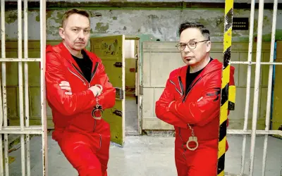 Dwóch mężczyzn w czerwonych kombinezonach i kajdankach, gotowych do ucieczki. Czy uda im się unlock po polsku?