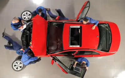 Mechanicy pracują przy czerwonym aucie. Jeden spisuje notatki, inny podłącza komputer diagnostyczny. Wszyscy skupieni, by zapobiec deprecjacji pojazdu.