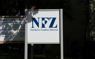 Tablica z logo NFZ i napisem Narodowy Fundusz Zdrowia. Obok tablica z informacjami o inwestycjach, jak sprawdzić oddział NFZ.