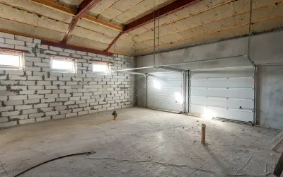 Intérieur d'un garage en construction, prêt à isoler. Murs en parpaings, plafond isolée, portes de garage sectionnelles blanches.