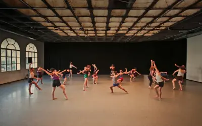 Grupa tancerzy wykonuje dynamiczny gaga taniec w przestronnej sali.